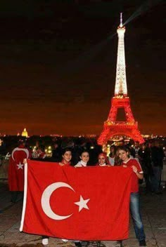 some people are holding a flag in front of the eiffel tower at night