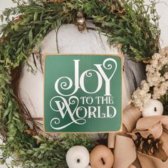 a green sign that says joy to the world surrounded by wreaths and other decorations