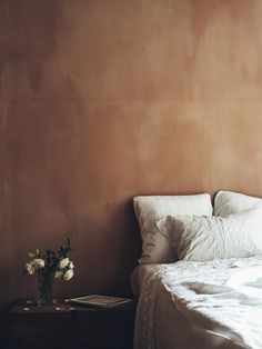 a white bed sitting next to a wooden table with flowers on it in front of a brown wall