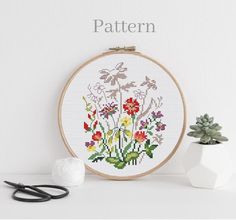 a cross stitch pattern with flowers on it next to scissors and a potted plant