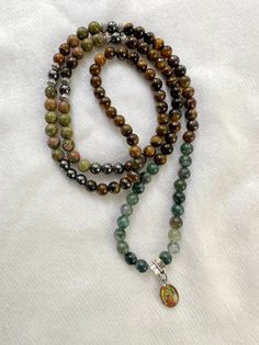 Elastic and mixed gemstome mala with the image of the Lady of Guadalupe. Gemstones are: Tiger Eye, Hematite, Unakite jasper and Moss Agate Can be wrapped around your wrist and worn as a bracelet. Comes in a velvet bag with a mini charm for storage and care. Information card also included. FROM MY SACRED SPACE TO YOURS: Every product goes through a cleansing and Reiki energy ritual the moment I prepare your order. Spiritual Jewelry With 8mm Round Beads, Spiritual Agate Mala With 108 Beads, Spiritual Green Hand-strung Crystal Necklaces, Adjustable Agate Hand-strung Mala, Spiritual Agate Crystal Necklace With Gemstone, Spiritual Agate Gemstone Crystal Necklace, Adjustable Hand-strung Agate Mala, Adjustable Agate Mala With 8mm Beads, Spiritual Adjustable Hand-strung Crystal Necklaces