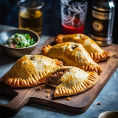 two meat empanadas on a cutting board next to a bowl of salad