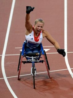 a woman in a wheel chair on a track raising her arm up to the sky