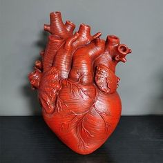 a red heart shaped sculpture sitting on top of a black table next to a gray wall