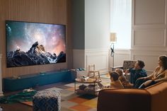 family sitting on couch watching tv in living room with large screen television mounted to the wall