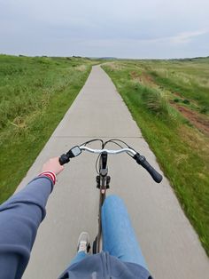 a person riding a bike down a road next to a lush green field on a cloudy day