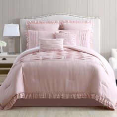 a bed with pink comforter and pillows on top of it in a white room