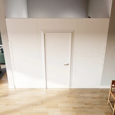 an empty chair sits in front of a white wall with two open doors on it