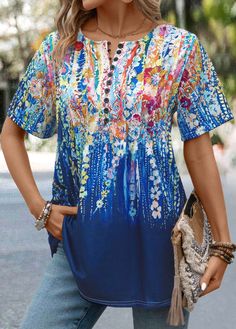 a woman wearing a blue top with colorful flowers and fringes on the front, standing in