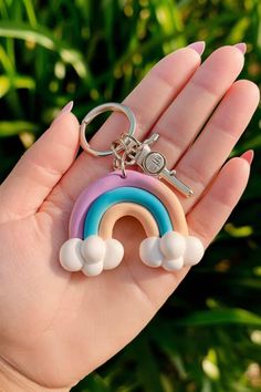 a hand holding a keychain that has a rainbow and clouds on it in front of some grass