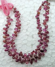 three strand necklace with pink beads and tassels on white background, closeup