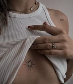 a woman with a sun tattoo on her chest holding onto a white t - shirt