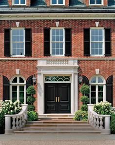 a large brick house with black shutters and white trim on the front entrance steps