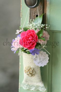 a pink rose hanging from a door handle on a green wooden door with lace and burlap