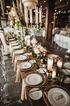 a long table is set with white plates and candles for an elegant dinner party or reception