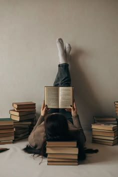 a woman laying on the floor reading a book next to piles of books with her legs up