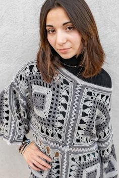 a woman standing in front of a wall wearing a black and white crochet sweater