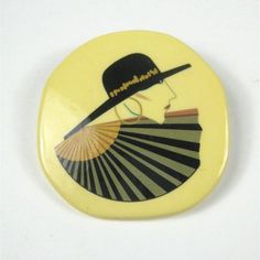 a button with an image of a woman wearing a hat and holding a fan in her hand