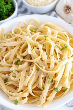 a white bowl filled with pasta and parsley on top of a marble countertop