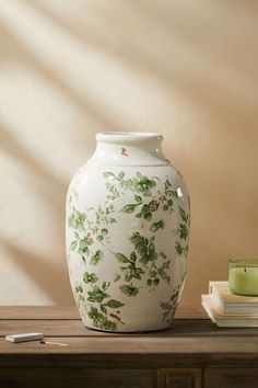 a white vase sitting on top of a wooden table next to a book and candle