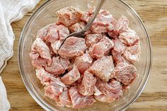 a glass bowl filled with raw meat on top of a wooden table