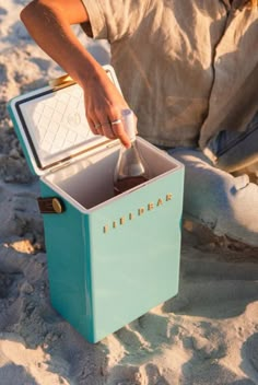 a person sitting in the sand with an ice chest