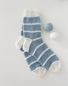 a pair of blue and white striped socks next to two balls of yarn