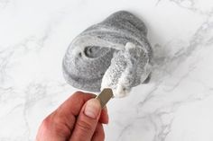 a hand is holding a toothbrush in front of a gray animal's head