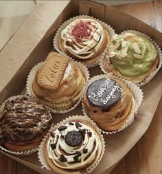 a box filled with lots of different flavored cupcakes on top of a wooden table