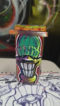 a cup with some graffiti on it sitting on a table next to a pencil drawing