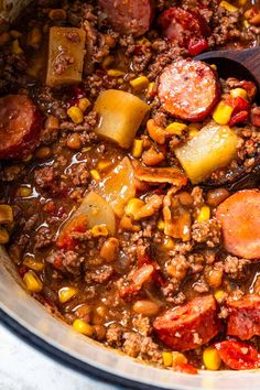 a pot filled with meat and vegetables next to a wooden spoon