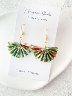 a pair of green and red leaf earrings sitting on top of a white plate next to a card