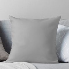 a white pillow sitting on top of a couch next to two gray pillows and a blanket