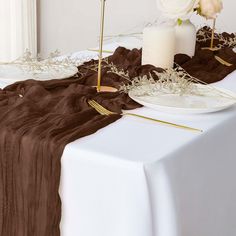 a table topped with a white vase filled with flowers next to a brown cloth covered table