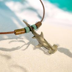 a silver shark necklace on a brown leather cord next to the ocean and blue water