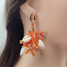 Brighten up your look with these Orange and White Coral Stud Earrings, expertly handcrafted from Japanese Delica beads. Each earring features detailed beaded coral branches and intricately beaded starfish in vibrant orange and crisp white tones. Enhanced with genuine seashells and 18K gold-filled accents, these earrings radiate both luxury and natural beauty. The 18K gold-filled stud closures, designed as delicate seashells, add a sophisticated finishing touch. Ideal for beach lovers and those w Orange Earrings For Beach With Pierced Ears, Orange Earrings For Beach, Adjustable Beaded Earrings With Dangling Beads For Beach, Bohemian Beaded Dangling Earrings For Vacation, Orange Drop Earrings For The Beach, Orange Drop Earrings For Beach, Bohemian Dangle Beaded Earrings For Vacation, Orange Dangle Earrings For The Beach, Orange Dangle Earrings For Beach