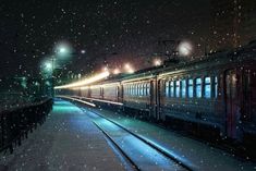 a train on the tracks at night with snow falling all over it and lights shining