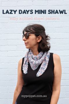 a woman standing in front of a white brick wall wearing sunglasses and a knitted shawl