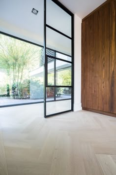 an empty room with wood floors and glass doors on the outside, looking out onto a garden