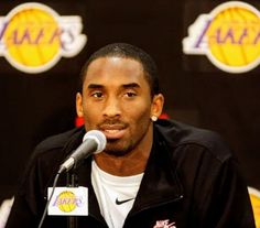 a man sitting in front of a microphone with lakers logos on it's wall behind him