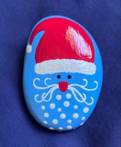 a painted rock with a santa claus hat on it's face and eyes, sitting on a blue surface