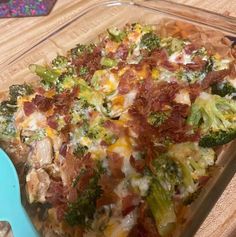 a casserole dish with broccoli, bacon and cheese on it next to a blue spoon