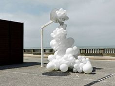 a bunch of white balloons that are in the air next to a basketball hoop and net