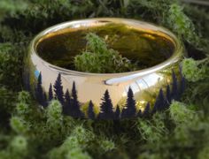 a ring with trees painted on it sitting in the grass next to some plants and moss