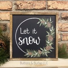 a sign that says let it snow in front of a brick wall with pine cones