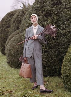 a man in a gray suit holding a brown bag and standing next to some bushes