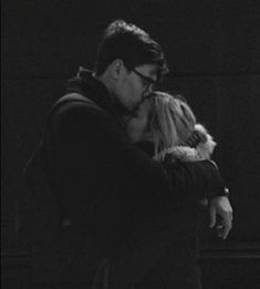 a black and white photo of a man kissing a woman's face in the dark