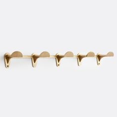 four brass hooks on a white wall with one hook in the shape of three hearts