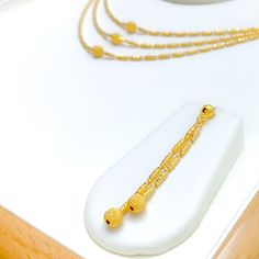 This Shimmering Triple Lara 22k Gold Set, weighing 22.0 grams, exudes timeless elegance and refined style. Crafted from the finest 22k gold, it features a warm yellow gold finish, highlighting the exquisite craftsmanship. The set includes a graceful triple-layered necklace, with the first row measuring 16 inches and the third row 17 inches, creating a sophisticated cascading effect. Secured with a lobster lock, it offers both durability and ease of wear. The set is complemented by matching earrings, each 2.25 inches in length, with push-back posts for comfortable fitting. Ideal for those seeking a harmonious blend of classic and contemporary design, this set is perfect for making a luxurious statement at any event. PRODUCT DETAILS Gold Purity(karat): 22k Gold Weight(grams): 22.0 Item Finis Elegant 22k Gold Temple Necklace With Gold Beads, Elegant 22k Gold Plated Necklaces, 22k Yellow Gold Temple Necklace With Gold Beads, 22k Gold Temple Necklace With Gold Beads, Elegant 22k Gold Necklaces, 22k Gold Beaded Jewelry For Formal Occasions, 22k Gold Beads Jewelry For Formal Occasions, 22k Gold Jewelry For Formal Occasions, 22k Yellow Gold Hallmarked Temple Necklace