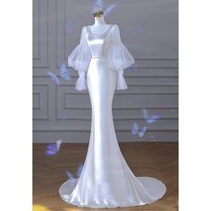 a white wedding dress on display with blue butterflies around the neck and sleeves, in front of a gray wall